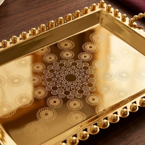 Add a touch of regal sophistication to your hosting with this exquisite 3-piece gold-plated stainless steel tray set. Featuring an intricate, laser-etched mandala design at the center and a decorative beaded "pearl" border, these trays blend traditional artistry with modern durability. The high-polish mirror finish reflects light beautifully, making them a stunning centerpiece for dining tables, coffee tables, or vanity displays. Whether you are serving refreshments to guests or organizing luxury accessories, this nesting set provides a versatile and opulent solution for any home. Key Features Premium Craftsmanship: Constructed from high-grade stainless steel with a brilliant gold-toned finish for long-lasting shine and rust resistance. Intricate Mandala Art: Each tray features a precision-etched geometric mandala pattern that adds a unique, artisanal feel to the collection. Ornate Beaded Edges: The scalloped rims are adorned with gold bead detailing, providing a secure grip and a sophisticated aesthetic. Versatile Set of Three: Includes small, medium, and large sizes that nest together for easy storage or can be used separately for multi-course serving. Multi-Purpose Decor: Ideal for serving appetizers, tea, and desserts, or used as a decorative base for candles, perfumes, and floral arrangements.
