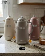 Three 1-liter DayDays thermal flasks in Dusty Rose, Warm Sand, and Stone Grey arranged on a granite kitchen countertop.