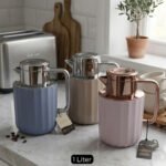 Three 1-liter Nordic-style thermal flasks in Slate Blue, Sand Beige, and Soft Rose colors with fluted textures and metallic lids displayed on a kitchen counter.