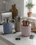 Three 1-liter Nordic-style thermal flasks in Slate Blue, Sand Beige, and Soft Rose colors with fluted textures and metallic lids displayed on a kitchen counter.
