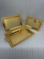 Add a touch of regal sophistication to your hosting with this exquisite 3-piece gold-plated stainless steel tray set. Featuring an intricate, laser-etched mandala design at the center and a decorative beaded "pearl" border, these trays blend traditional artistry with modern durability. The high-polish mirror finish reflects light beautifully, making them a stunning centerpiece for dining tables, coffee tables, or vanity displays. Whether you are serving refreshments to guests or organizing luxury accessories, this nesting set provides a versatile and opulent solution for any home. Key Features Premium Craftsmanship: Constructed from high-grade stainless steel with a brilliant gold-toned finish for long-lasting shine and rust resistance. Intricate Mandala Art: Each tray features a precision-etched geometric mandala pattern that adds a unique, artisanal feel to the collection. Ornate Beaded Edges: The scalloped rims are adorned with gold bead detailing, providing a secure grip and a sophisticated aesthetic. Versatile Set of Three: Includes small, medium, and large sizes that nest together for easy storage or can be used separately for multi-course serving. Multi-Purpose Decor: Ideal for serving appetizers, tea, and desserts, or used as a decorative base for candles, perfumes, and floral arrangements.