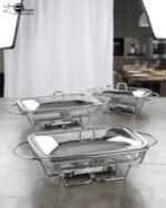 Three elegant Paramount Series food warmers in different sizes (1.5L, 2.4L, and 3L) featuring stainless steel lids and glass dishes with candle-lit buffet burners on a dining table.