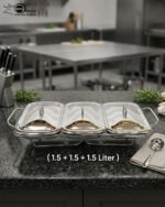 A professional Paramount Series 3-in-1 stainless steel food warmer with three 1.5L glass containers and polished metal lids, displayed on a kitchen counter and a dining table with various dishes.