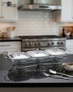 A Paramount Series 3-in-1 buffet food warmer featuring three square glass serving dishes with stainless steel lids on a chrome wire rack, displayed on a kitchen counter and an outdoor dining table with tea light candles lit underneath.