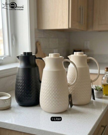 A 1-liter insulated thermal flask with a 3D diamond-patterned matte body, featuring a curved handle and a spout, shown in black and beige color options on a kitchen countertop.