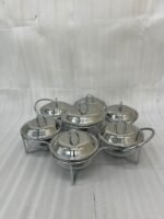 Paramount Series 7-in-1 buffet food warmer set featuring seven clear glass bowls with polished stainless steel lids and a silver metal stand with buffet burners on a decorated dining table.