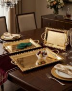 Add a touch of regal sophistication to your hosting with this exquisite 3-piece gold-plated stainless steel tray set. Featuring an intricate, laser-etched mandala design at the center and a decorative beaded "pearl" border, these trays blend traditional artistry with modern durability. The high-polish mirror finish reflects light beautifully, making them a stunning centerpiece for dining tables, coffee tables, or vanity displays. Whether you are serving refreshments to guests or organizing luxury accessories, this nesting set provides a versatile and opulent solution for any home. Key Features Premium Craftsmanship: Constructed from high-grade stainless steel with a brilliant gold-toned finish for long-lasting shine and rust resistance. Intricate Mandala Art: Each tray features a precision-etched geometric mandala pattern that adds a unique, artisanal feel to the collection. Ornate Beaded Edges: The scalloped rims are adorned with gold bead detailing, providing a secure grip and a sophisticated aesthetic. Versatile Set of Three: Includes small, medium, and large sizes that nest together for easy storage or can be used separately for multi-course serving. Multi-Purpose Decor: Ideal for serving appetizers, tea, and desserts, or used as a decorative base for candles, perfumes, and floral arrangements.