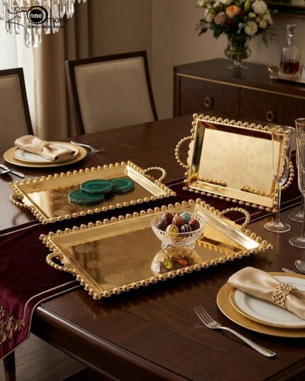 Add a touch of regal sophistication to your hosting with this exquisite 3-piece gold-plated stainless steel tray set. Featuring an intricate, laser-etched mandala design at the center and a decorative beaded "pearl" border, these trays blend traditional artistry with modern durability. The high-polish mirror finish reflects light beautifully, making them a stunning centerpiece for dining tables, coffee tables, or vanity displays. Whether you are serving refreshments to guests or organizing luxury accessories, this nesting set provides a versatile and opulent solution for any home. Key Features Premium Craftsmanship: Constructed from high-grade stainless steel with a brilliant gold-toned finish for long-lasting shine and rust resistance. Intricate Mandala Art: Each tray features a precision-etched geometric mandala pattern that adds a unique, artisanal feel to the collection. Ornate Beaded Edges: The scalloped rims are adorned with gold bead detailing, providing a secure grip and a sophisticated aesthetic. Versatile Set of Three: Includes small, medium, and large sizes that nest together for easy storage or can be used separately for multi-course serving. Multi-Purpose Decor: Ideal for serving appetizers, tea, and desserts, or used as a decorative base for candles, perfumes, and floral arrangements.