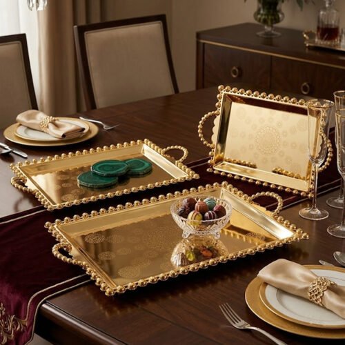 Add a touch of regal sophistication to your hosting with this exquisite 3-piece gold-plated stainless steel tray set. Featuring an intricate, laser-etched mandala design at the center and a decorative beaded "pearl" border, these trays blend traditional artistry with modern durability. The high-polish mirror finish reflects light beautifully, making them a stunning centerpiece for dining tables, coffee tables, or vanity displays. Whether you are serving refreshments to guests or organizing luxury accessories, this nesting set provides a versatile and opulent solution for any home. Key Features Premium Craftsmanship: Constructed from high-grade stainless steel with a brilliant gold-toned finish for long-lasting shine and rust resistance. Intricate Mandala Art: Each tray features a precision-etched geometric mandala pattern that adds a unique, artisanal feel to the collection. Ornate Beaded Edges: The scalloped rims are adorned with gold bead detailing, providing a secure grip and a sophisticated aesthetic. Versatile Set of Three: Includes small, medium, and large sizes that nest together for easy storage or can be used separately for multi-course serving. Multi-Purpose Decor: Ideal for serving appetizers, tea, and desserts, or used as a decorative base for candles, perfumes, and floral arrangements.