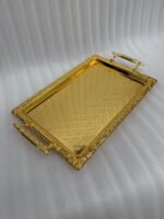 A luxury three-piece set of rectangular gold-plated stainless steel serving trays with intricate floral embossing and ornate vintage handles, displayed on a wooden dining table with elegant place settings.