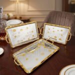 A set of three luxury Onemore brand stainless steel serving trays with gold-textured handles and borders, featuring etched floral patterns on a mirror-polished surface, displayed on a dark wooden dining table.