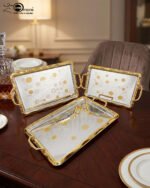 A set of three luxury Onemore brand stainless steel serving trays with gold-textured handles and borders, featuring etched floral patterns on a mirror-polished surface, displayed on a dark wooden dining table.