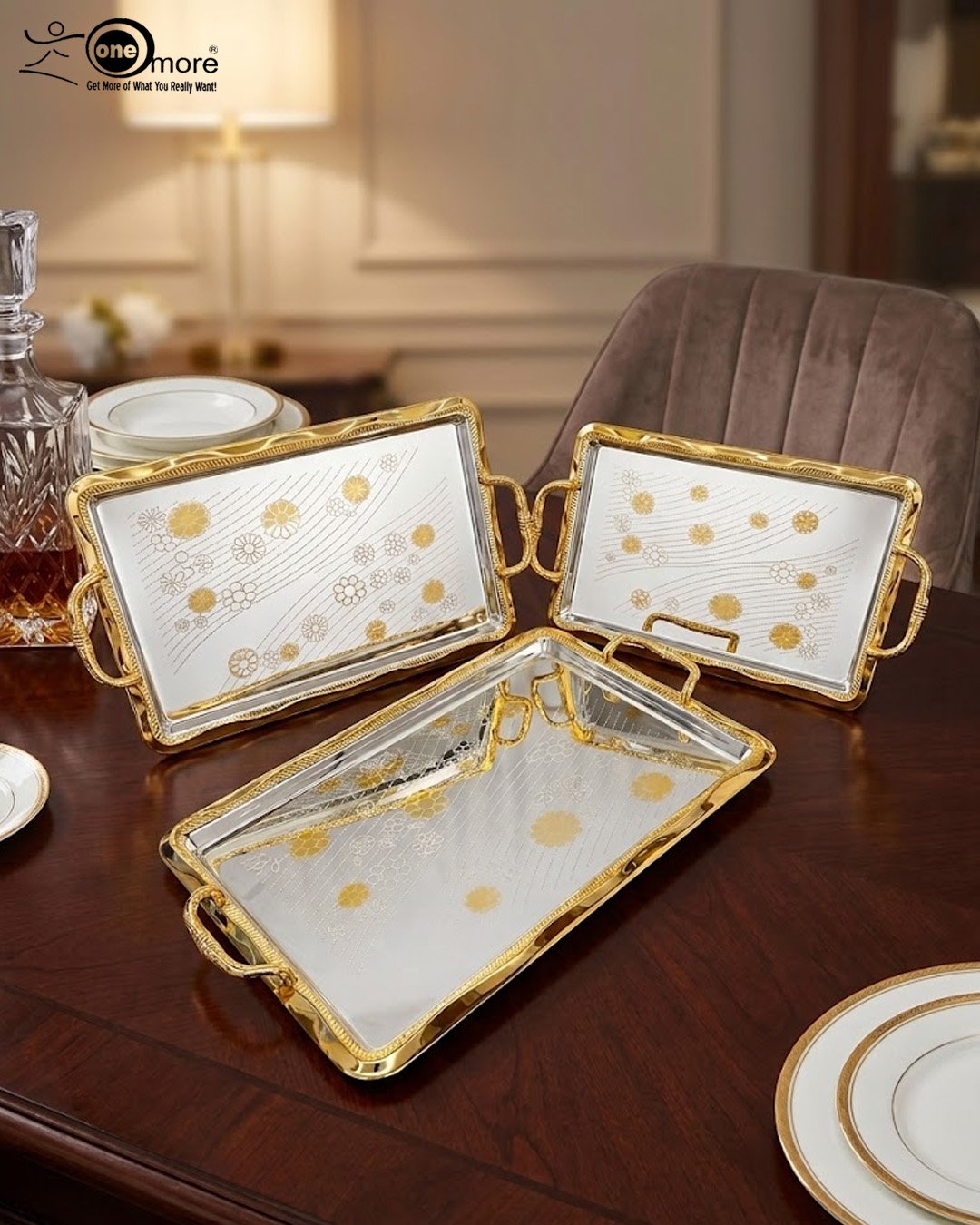 2 A set of three luxury Onemore brand stainless steel serving trays with gold-textured handles and borders, featuring etched floral patterns on a mirror-polished surface, displayed on a dark wooden dining table.