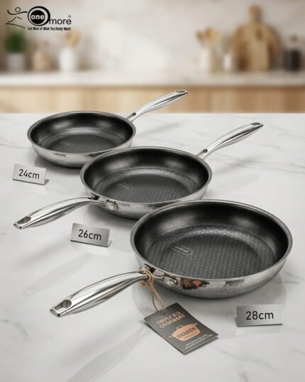 A set of three UAKEEN premium tri-ply stainless steel fry pans with laser-etched honeycomb non-stick interiors, shown in 24cm, 26cm, and 28cm sizes on a marble countertop with an induction-compatible base.