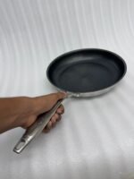 A set of three UAKEEN premium tri-ply stainless steel fry pans with laser-etched honeycomb non-stick interiors, shown in 24cm, 26cm, and 28cm sizes on a marble countertop with an induction-compatible base.