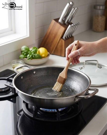 High-angle shot of two Uakeen stainless steel non-stick woks in 30cm and 32cm sizes on a wooden countertop, showing the laser-etched hexagonal interior and tempered glass lids.