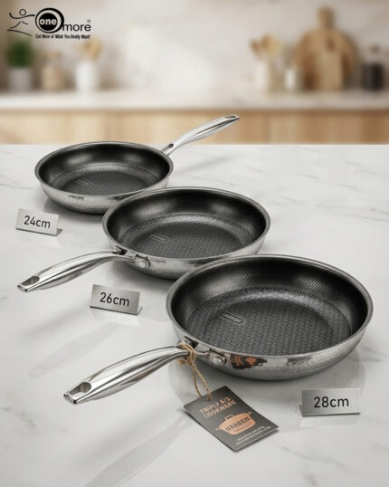 A set of three UAKEEN premium tri-ply stainless steel fry pans with laser-etched honeycomb non-stick interiors, shown in 24cm, 26cm, and 28cm sizes on a marble countertop with an induction-compatible base.