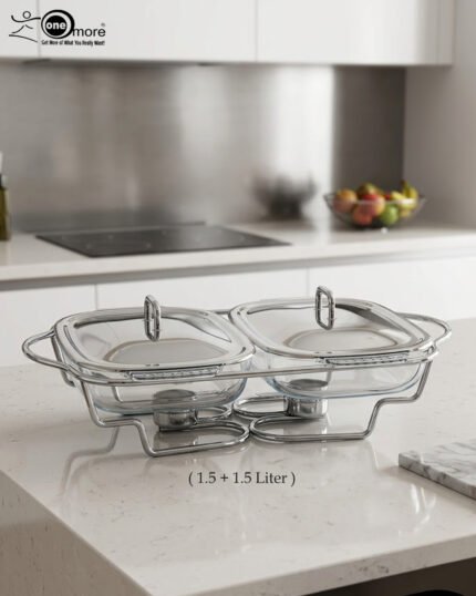 A Paramount Series double stainless steel food warmer on a dining table, featuring two 1.5L glass dishes with lids being lifted to reveal steaming food, supported by a chrome frame with two lit buffet burners underneath.