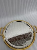 Set of three round silver stainless steel serving trays with floral etched patterns, gold rope borders, and ornate gold handles on a wooden dining table.