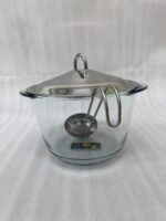 A 4-liter Paramount Series food warmer featuring a clear glass bowl, stainless steel stand, and lid, shown on a dining table with guests and filled with warm lentil soup.