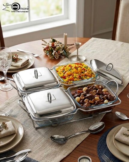 A luxurious Paramount Series 5-in-1 food warmer set on a wooden dining table, featuring four 2.5L glass serving dishes with polished stainless steel lids and tealight buffet burners underneath.