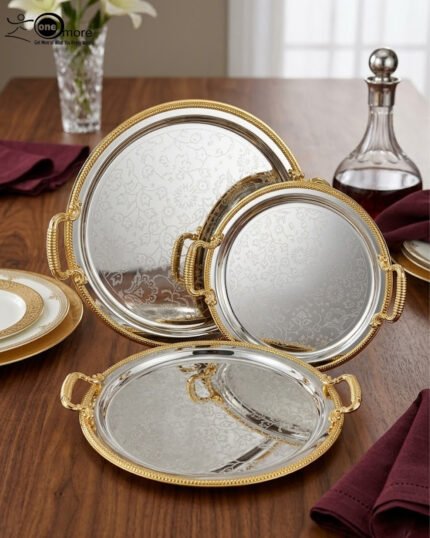 Set of three round silver stainless steel serving trays with floral etched patterns, gold rope borders, and ornate gold handles on a wooden dining table.