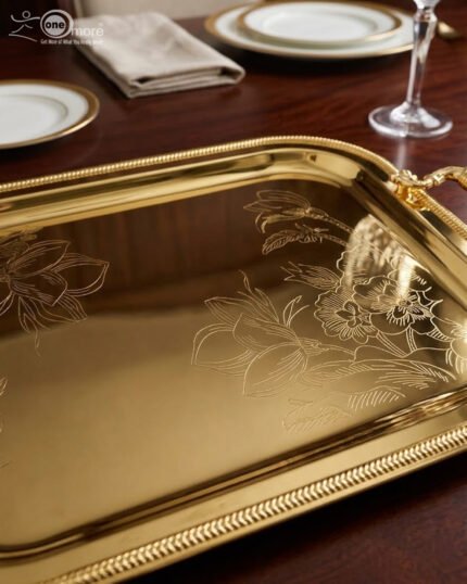 Three-piece set of luxury gold-plated stainless steel serving trays with intricate floral engravings and textured handles, displayed on a formal dining table.
