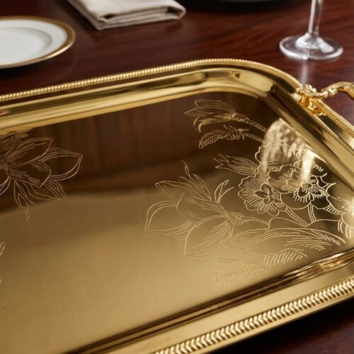 Three-piece set of luxury gold-plated stainless steel serving trays with intricate floral engravings and textured handles, displayed on a formal dining table.