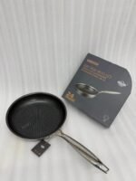 A set of three UAKEEN premium tri-ply stainless steel fry pans with laser-etched honeycomb non-stick interiors, shown in 24cm, 26cm, and 28cm sizes on a marble countertop with an induction-compatible base.