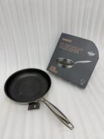A set of three UAKEEN premium tri-ply stainless steel fry pans with laser-etched honeycomb non-stick interiors, shown in 24cm, 26cm, and 28cm sizes on a marble countertop with an induction-compatible base.