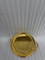 A luxury set of three circular 18K gold-plated stainless steel serving trays featuring intricate floral engravings and ornate handles, displayed on a white runner over a wooden table.