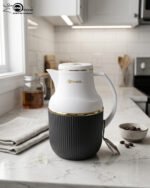 Three 1-liter Feenik thermal flasks in charcoal, taupe, and gray colors with gold trim on a marble kitchen countertop.