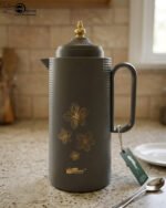 Three 1-liter DayDays insulated flasks in white, taupe, and grey, featuring gold floral designs and decorative gold lids on a kitchen counter.