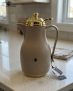 Three 1-liter thermal flasks in grey, beige, and white featuring matte finishes, elegant gold lids, and ergonomic handles on a marble countertop.