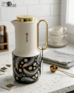 A trio of Feenik 1-liter luxury thermal flasks in cream with gold handles and lids, featuring three different artistic patterns on the base, displayed on a white marble kitchen counter.
