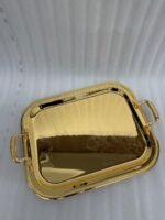 Three-piece set of luxury gold-plated stainless steel serving trays with intricate floral engravings and textured handles, displayed on a formal dining table.