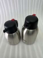 Stainless Steel Thermal Flask with a black lid and handle, available in 1.5 liter and 2 liter sizes, shown on a kitchen countertop.