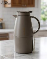 Three 2-liter luxury stainless steel thermal flasks in black, cream, and grey finishes with metallic handles, arranged on a white marble kitchen counter.