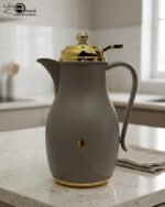 Three 1-liter thermal flasks in grey, beige, and white featuring matte finishes, elegant gold lids, and ergonomic handles on a marble countertop.