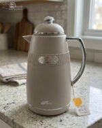 Three 1-liter DayDays thermal flasks in Dusty Rose, Warm Sand, and Stone Grey arranged on a granite kitchen countertop.