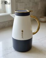 Three elegant 1.5-liter stainless steel thermal flasks in rose gold, slate grey, and charcoal blue bases with white bodies and gold-plated handles, displayed on a marble kitchen countertop.