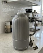 A collection of three 1-liter Feenik thermal flasks featuring a vertical ribbed design in beige, gray, and taupe on a white marble countertop.