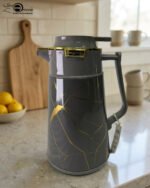 Three elegant 1-liter vacuum flasks in black, grey, and cream colors, featuring a golden Kintsugi-inspired marble pattern on a kitchen countertop.