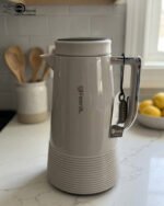 A trio of Feenik 1-liter thermal vacuum flasks in cream, sand grey, and mocha colors, displayed on a marble kitchen countertop.
