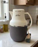 Three 1-liter modern vacuum flasks with cream-colored tops and ribbed bases in brown, grey, and beige, displayed on a white marble kitchen countertop.