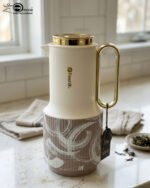 A trio of Feenik 1-liter luxury thermal flasks in cream with gold handles and lids, featuring three different artistic patterns on the base, displayed on a white marble kitchen counter.