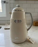 Three 1-liter DayDays thermal flasks in Dusty Rose, Warm Sand, and Stone Grey arranged on a granite kitchen countertop.