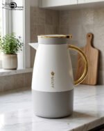 Three elegant 1.5-liter stainless steel thermal flasks in rose gold, slate grey, and charcoal blue bases with white bodies and gold-plated handles, displayed on a marble kitchen countertop.