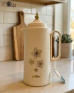 Three 1-liter DayDays insulated flasks in white, taupe, and grey, featuring gold floral designs and decorative gold lids on a kitchen counter.