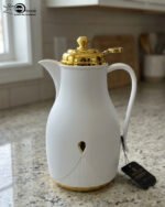 Three 1-liter thermal flasks in grey, beige, and white featuring matte finishes, elegant gold lids, and ergonomic handles on a marble countertop.